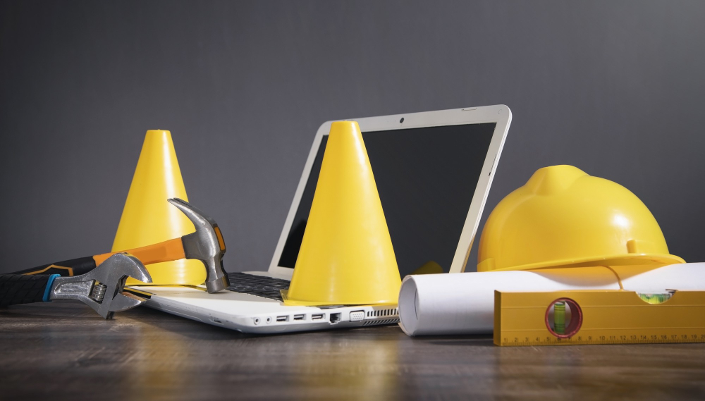 Cône de signalisation jaune, casque, document, marteau, clé avec un ordinateur portable.  En construction